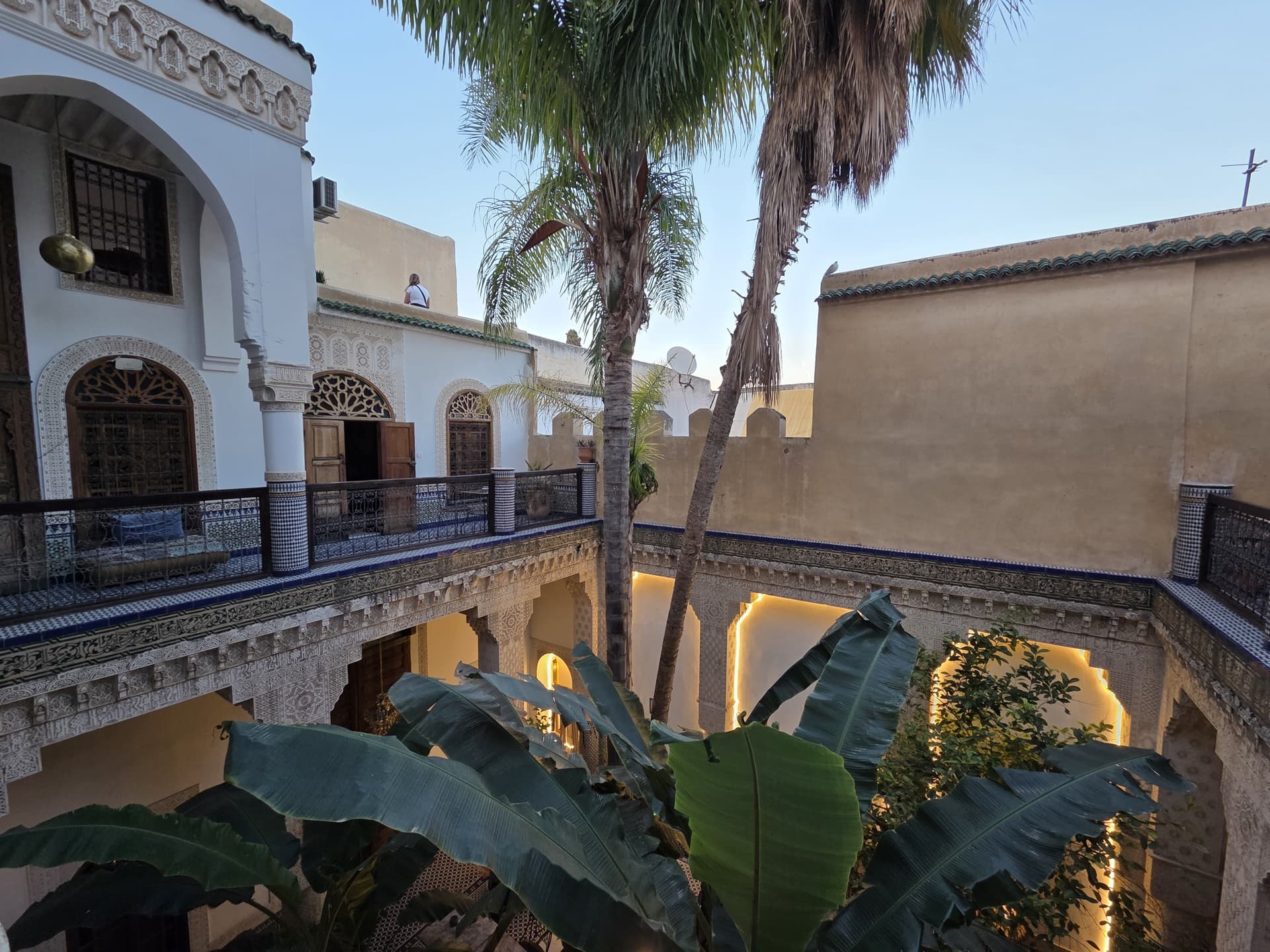 Sunlit riad courtyard in Fes with palm trees and mosaic tiling